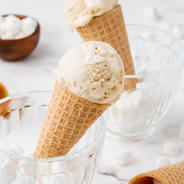 two sugar cones of marshmallow ice cream set in glass mugs filled with mini marshmallows.