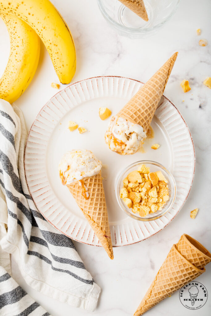 a white scalloped plate holding two sugar cones of banoffee pie ice cream and a dish of crushed vanilla wafers.