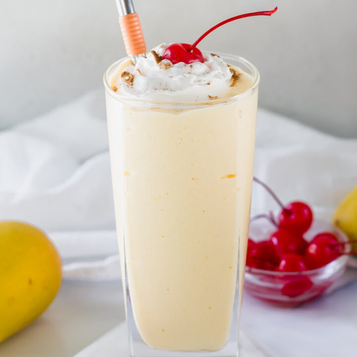 mango milkshake in a glass with a cherry and metal straw