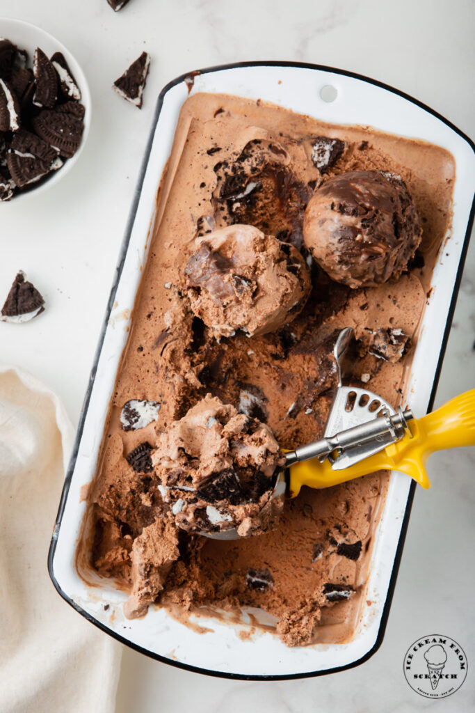 a white loaf pan filled with mississippi mud ice cream, being scooped with a yellow and metal ice cream scoop.