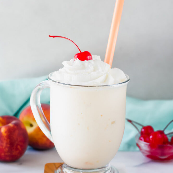 peach milkshake in a clear glass with a straw