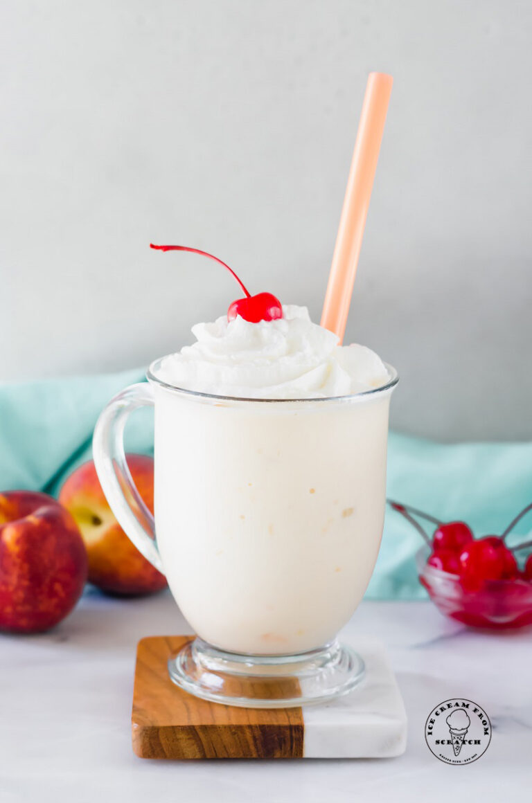 peach milkshake in a clear glass with a straw