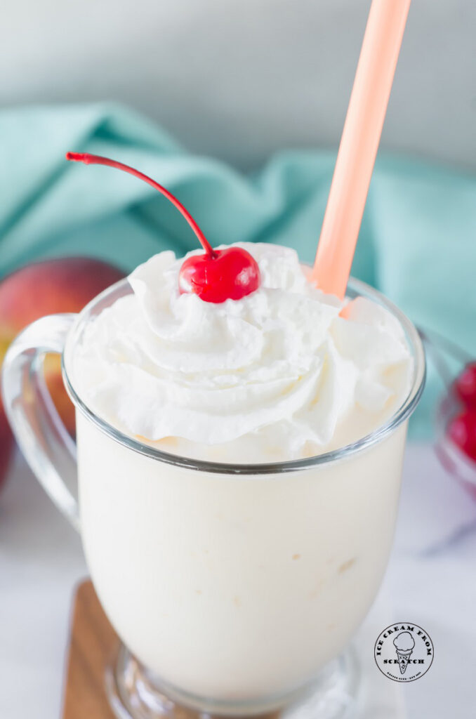 close up of a peach milkshake in a clear glass topped with a cherry
