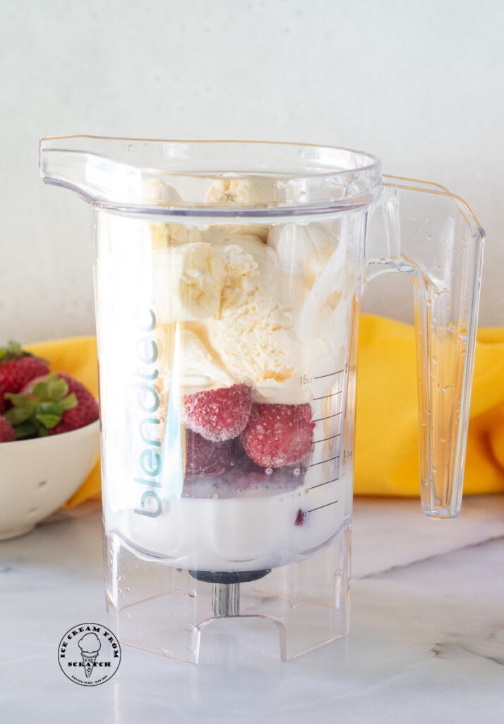 ingredients for a strawberry banana milkshake in a blender jar