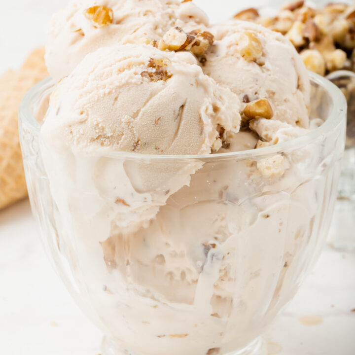 black walnut ice cream, multiple scoops in a glass ice cream dish, topped with chopped walnuts.