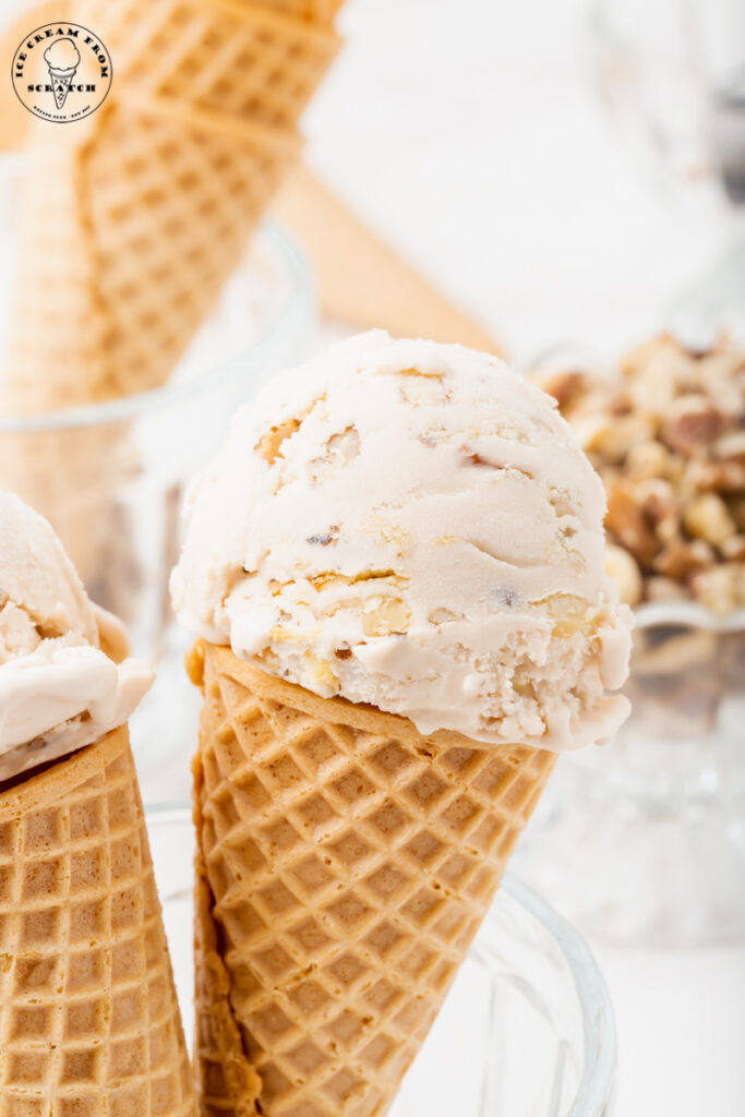 two sugar cones topped with a scoop of walnut ice cream, propped up in a glass dish.