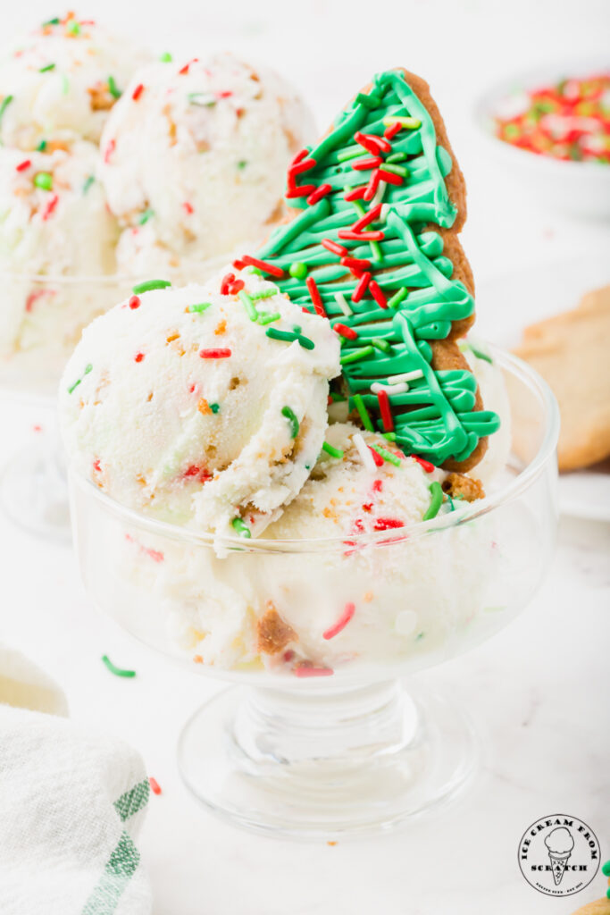 a wide, short, glass ice cream dish with scoops of christmas ice cream and a green frosted tree cookie topper.