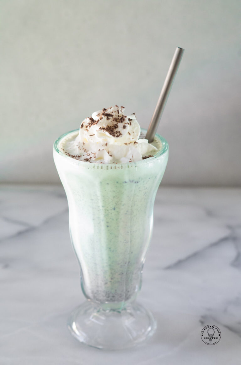 mint chocolate chip milkshake in a clear glass with a metal straw