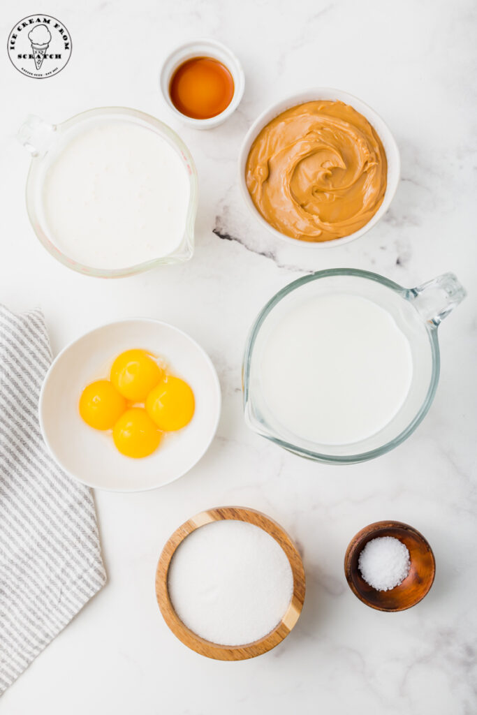 top down view of the ingredients needed to make homemade peanut butter ice cream, all in separate bowls on a white marble countertop.
