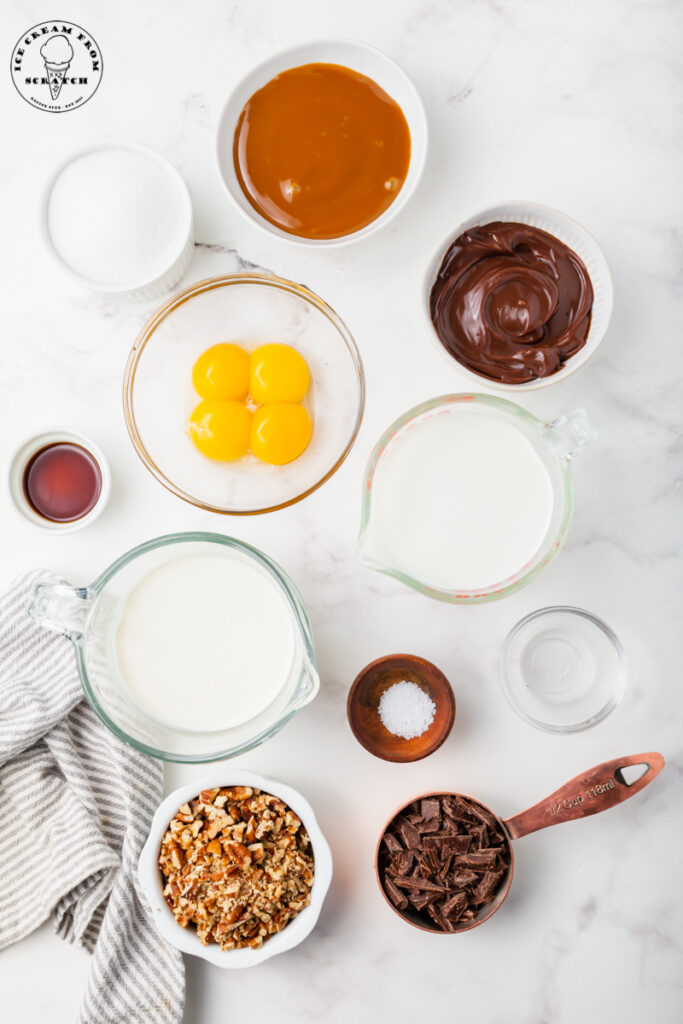 All of the ingredients for making homemade turtle ice cream are in separate bowls, measured out on a marble countertop.