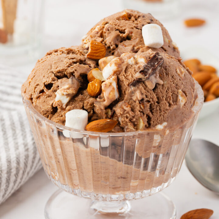 a glass footed dish filled with scoops of chocolate rocky road ice cream and topped with almonds and mini marshmallows