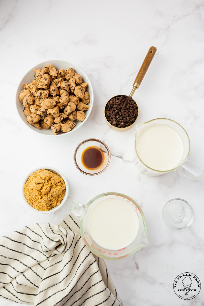 Ingredients needed for making cookie dough ice cream from scratch, all in separate bowls on a marble counter.