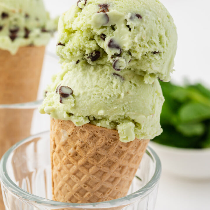 a sugar cone propped up in a glass, topped with two scoops of mint chocolate chip ice cream.
