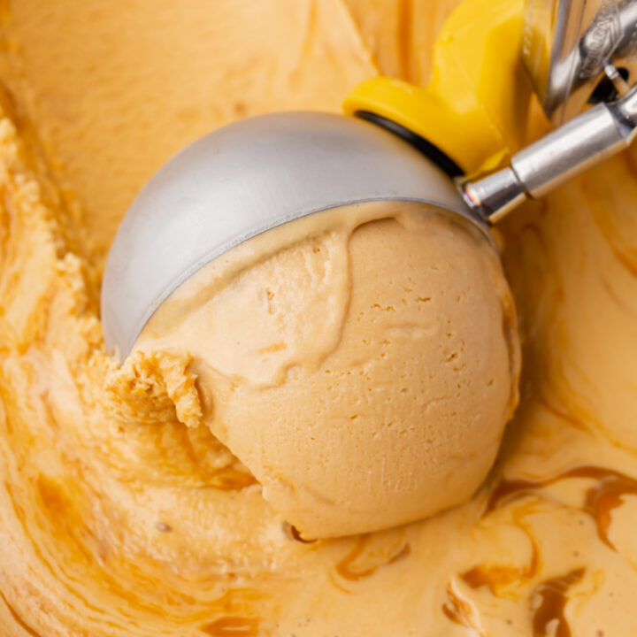 Homemade dulce de leche ice cream with caramel swirl, being scooped with a metal ice cream scoop.