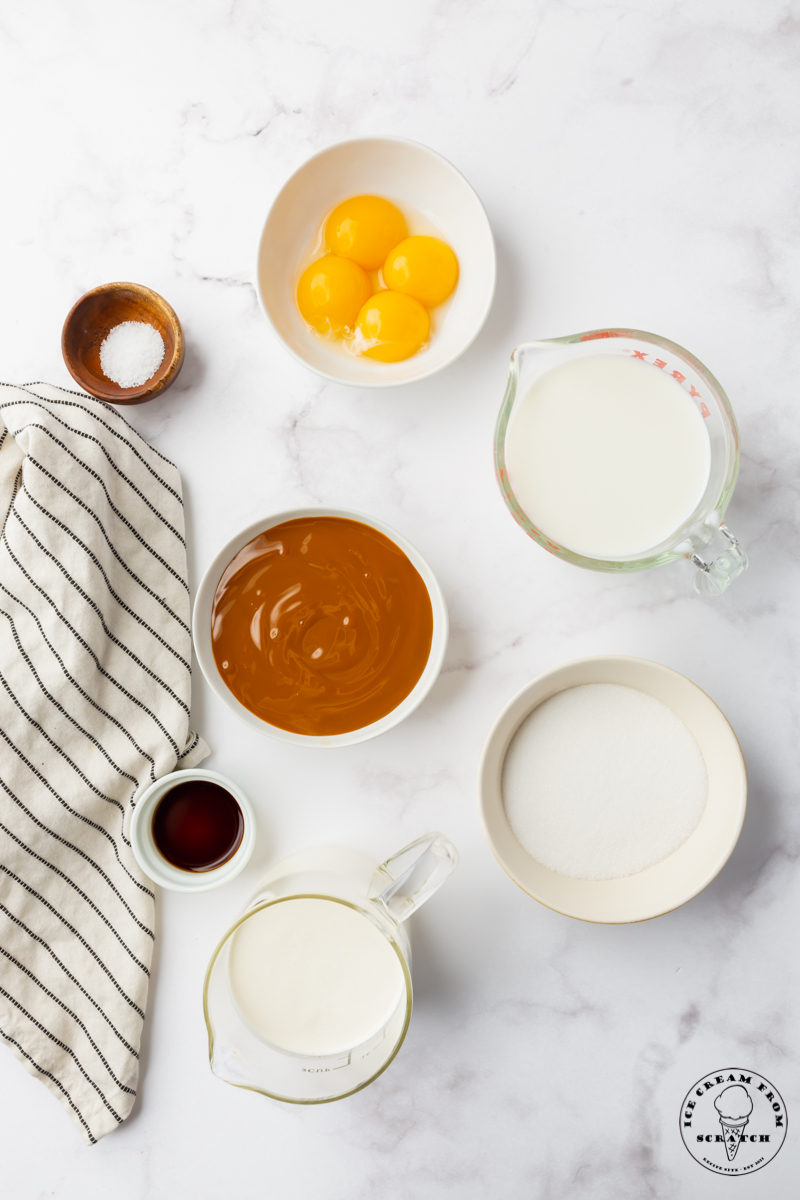 All of the ingredients that go into dulce de leche ice cream, measured into separate bowls, on a marble counter, viewed from above.