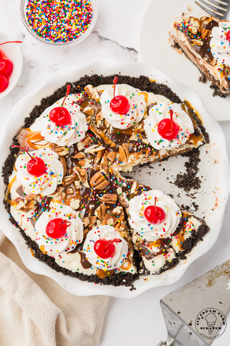 A whole ice cream pie with whipped cream and cherries. It's been sliced, and one slice has been removed.
