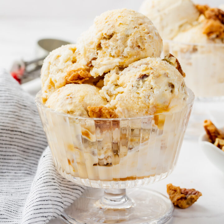 a footed glass dish filled with scoops of pralines and cream ice cream with praline candies scattered around.