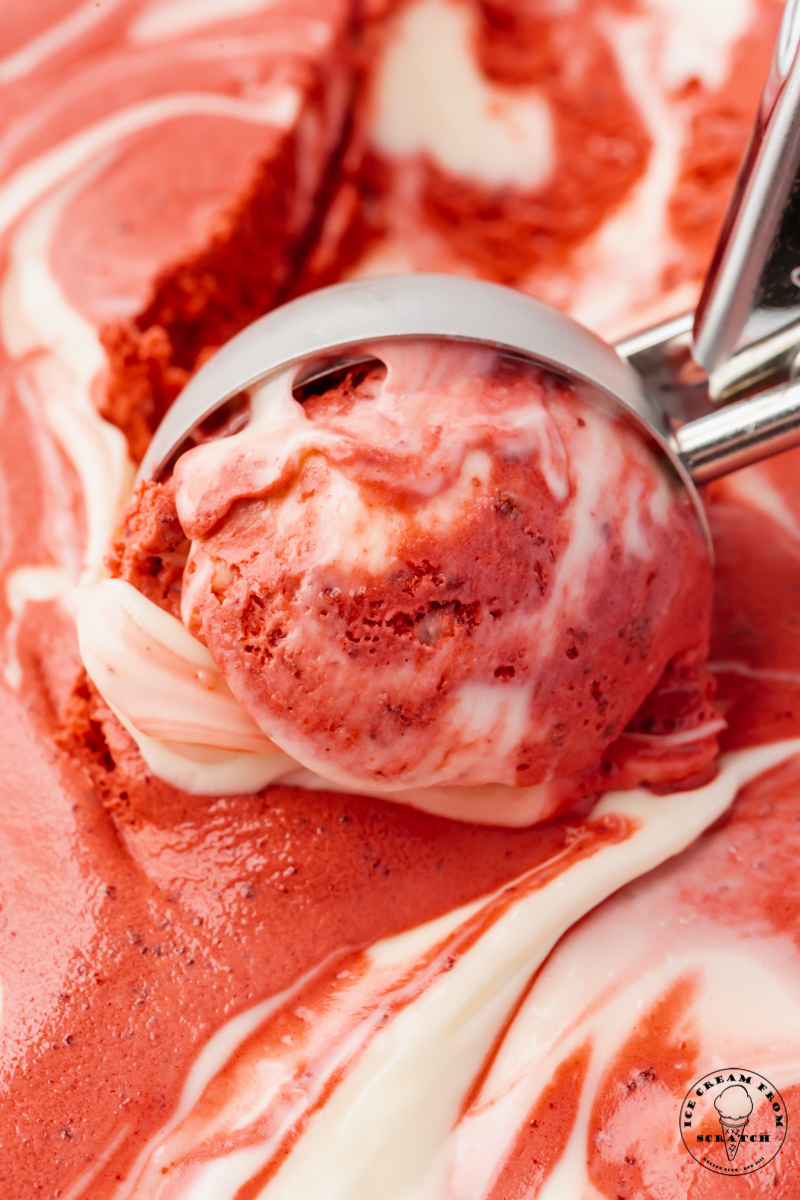 Red and white swirled red velvet ice cream, viewed from close up as it's scooped with an ice cream scoop