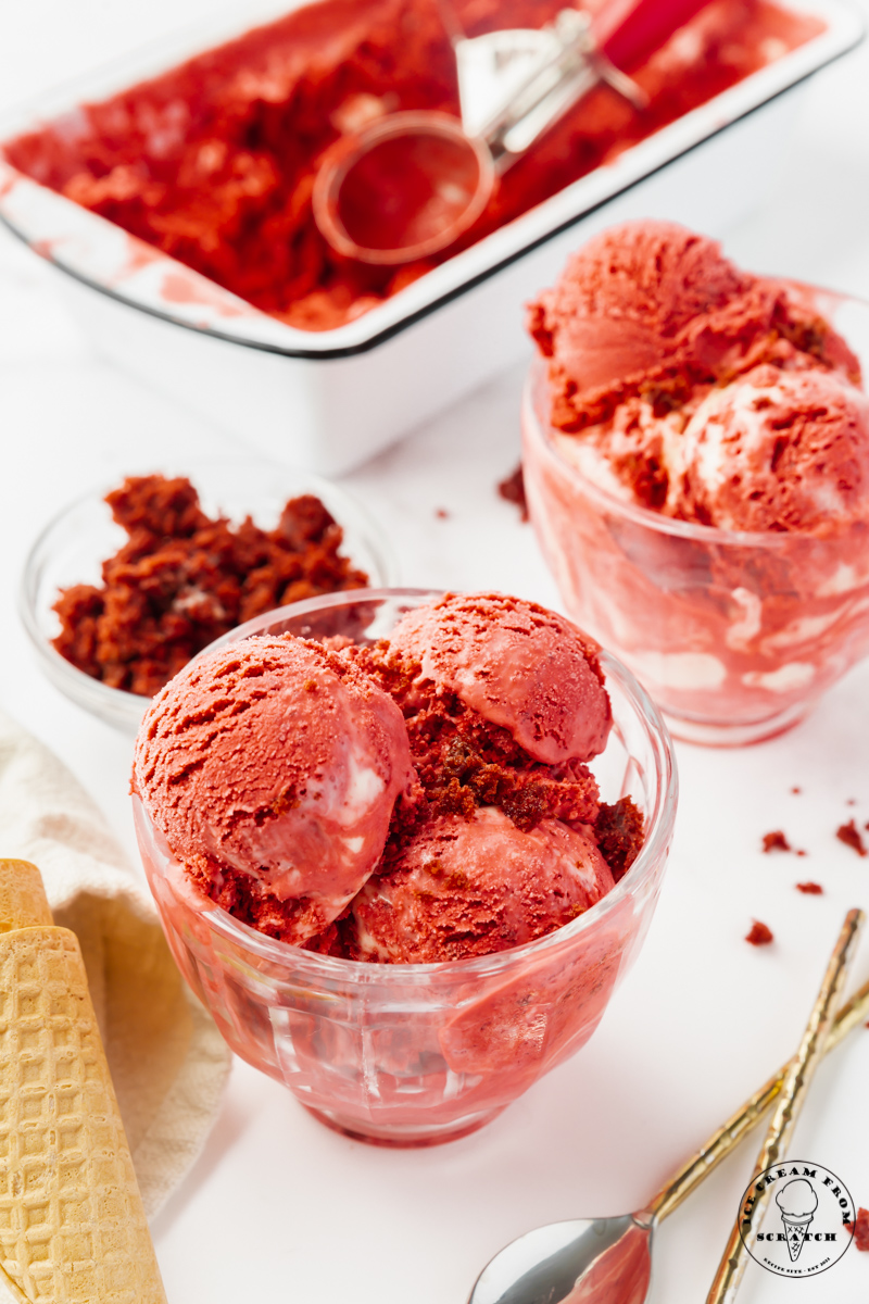 twp glass bowls of red velvet ice cream on a counter. In the background is a bread pan filled with homemade ice cream.