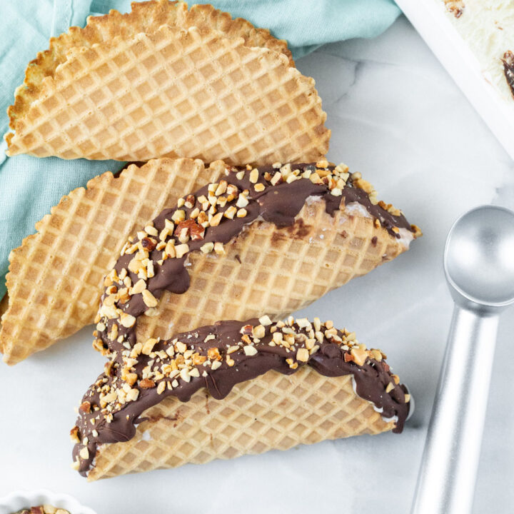 two choco tacos next to waffle shells chopped nuts and an ice cream scoop