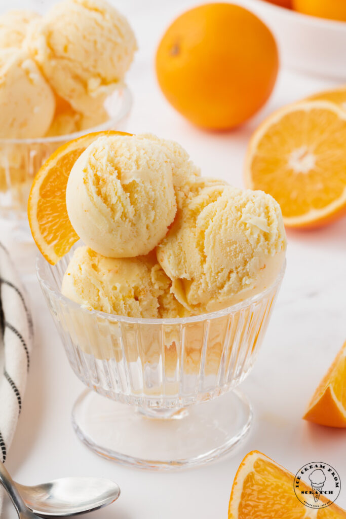 a ridged glass ice cream dish filled with scoops of homemade orange ice cream, garnished with an orange slice.