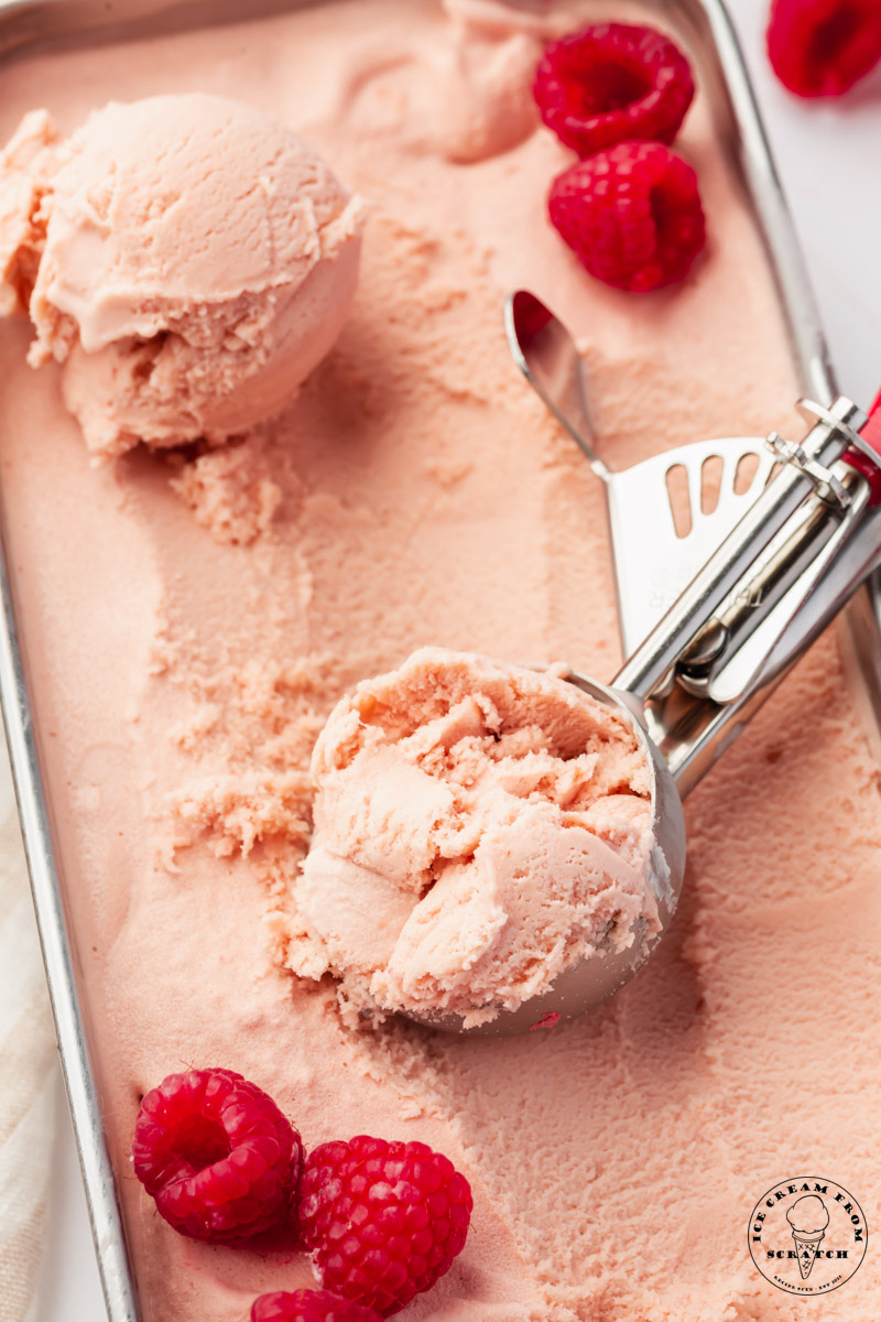 a metal bread pan filled with homemade raspberry ice cream, garnished with fresh berries.