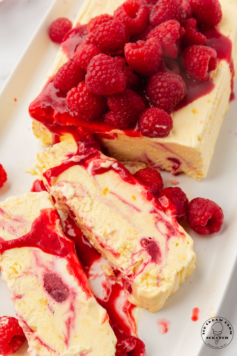 A sliced raspberry swirled semifreddo on a platter, topped with raspberries.