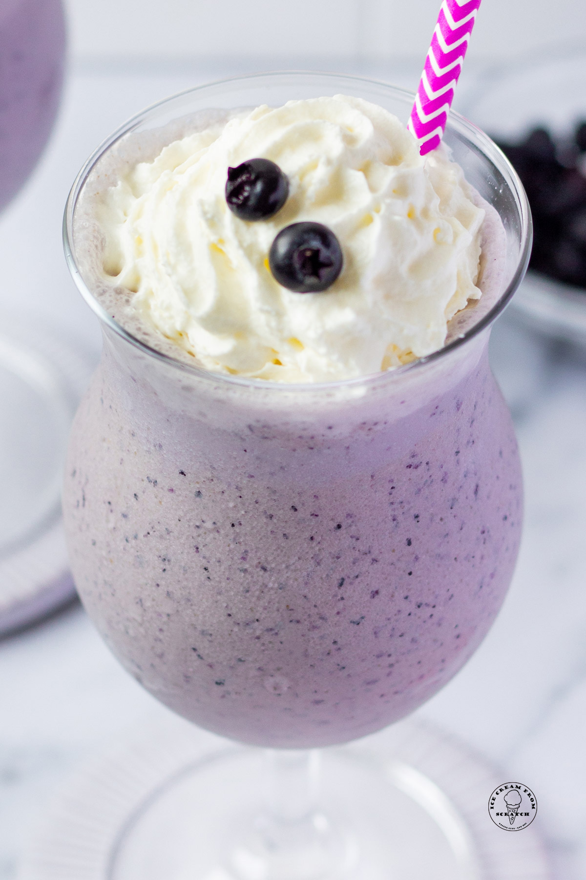 looking down into a glass filled with blueberry milkshake, topped with whipped cream and two fresh blueberries