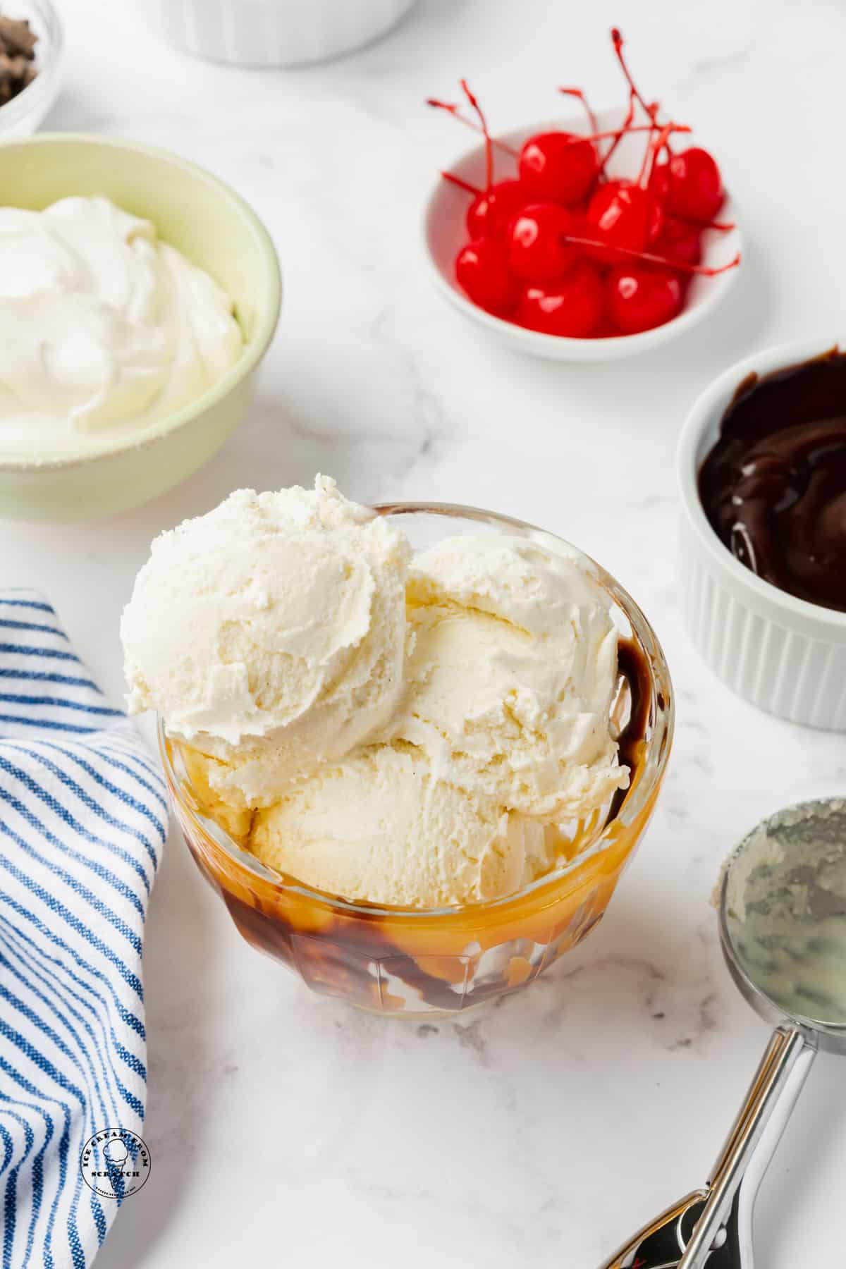 a bowl of vanilla ice cream. Sundae toppings are in small bowls behind it. 