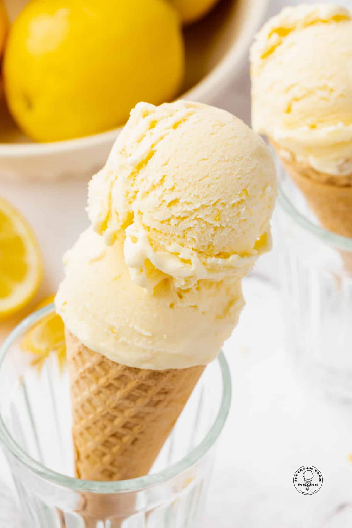 a sugar cone topped with two scoops of lemon ice cream, propped up in a glass.