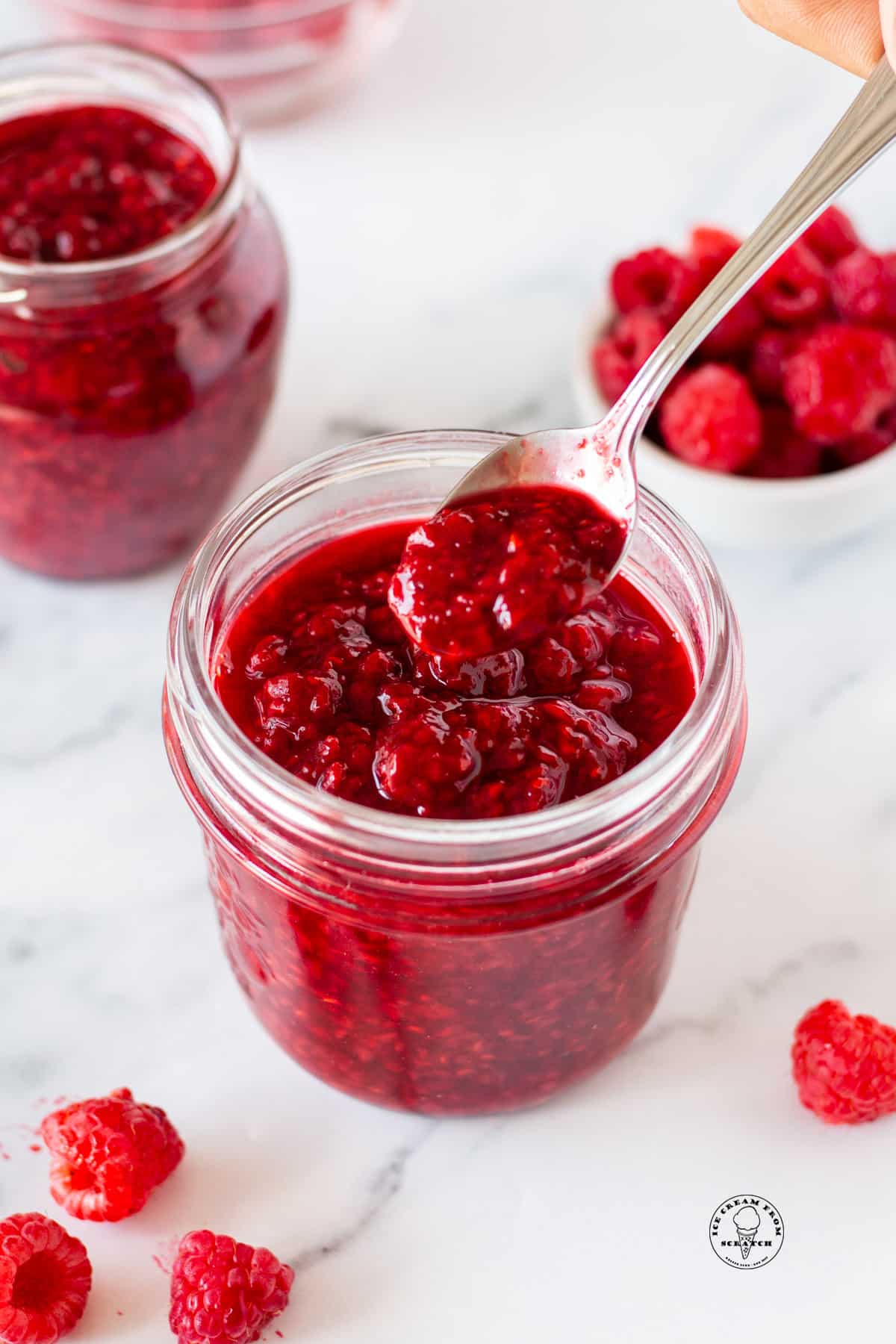a small mason jar filled with fresh raspberry compote. A small spoon is holding some up.