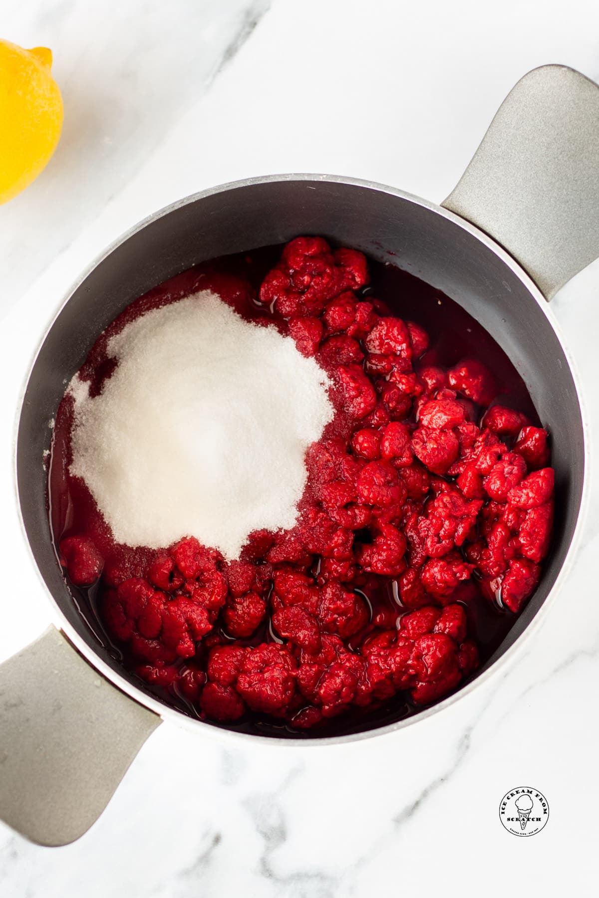 a metal saucepan holding thawed raspberries, sugar, and lemon juice
