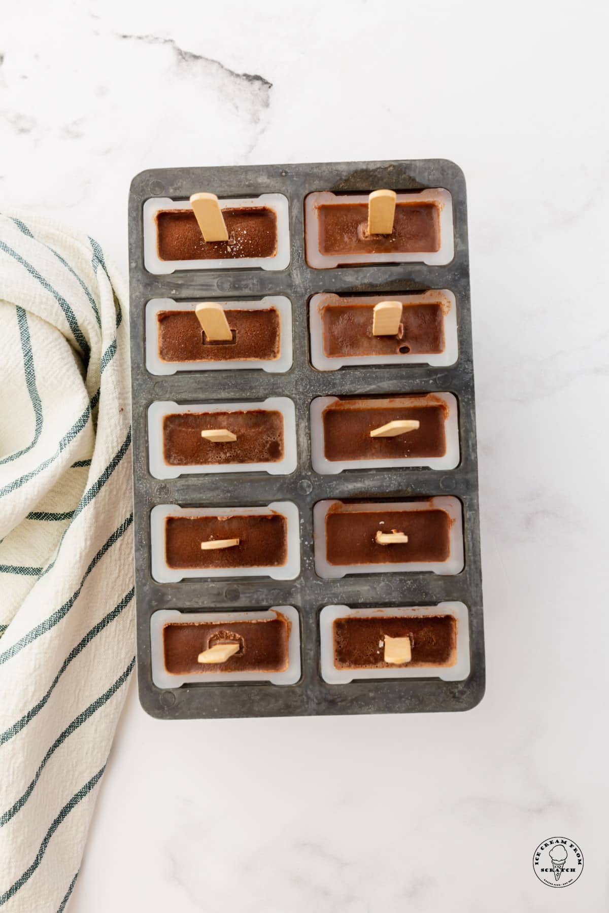 a ten-slot metal popsicle mold filled with fudgesicles, viewed from above.
