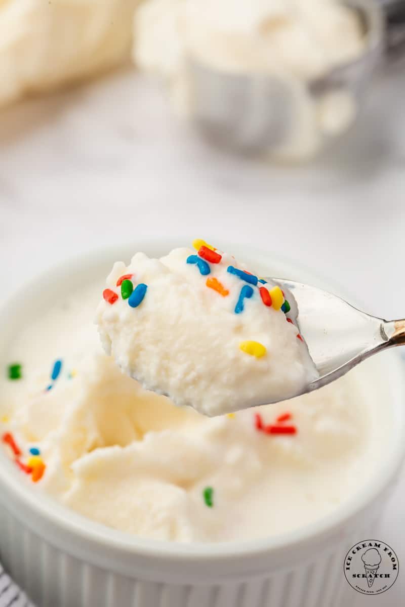 a spoon holding a bite of ice cream made in a bag to show the creamy texture. There are rainbow sprinkles on the ice cream.