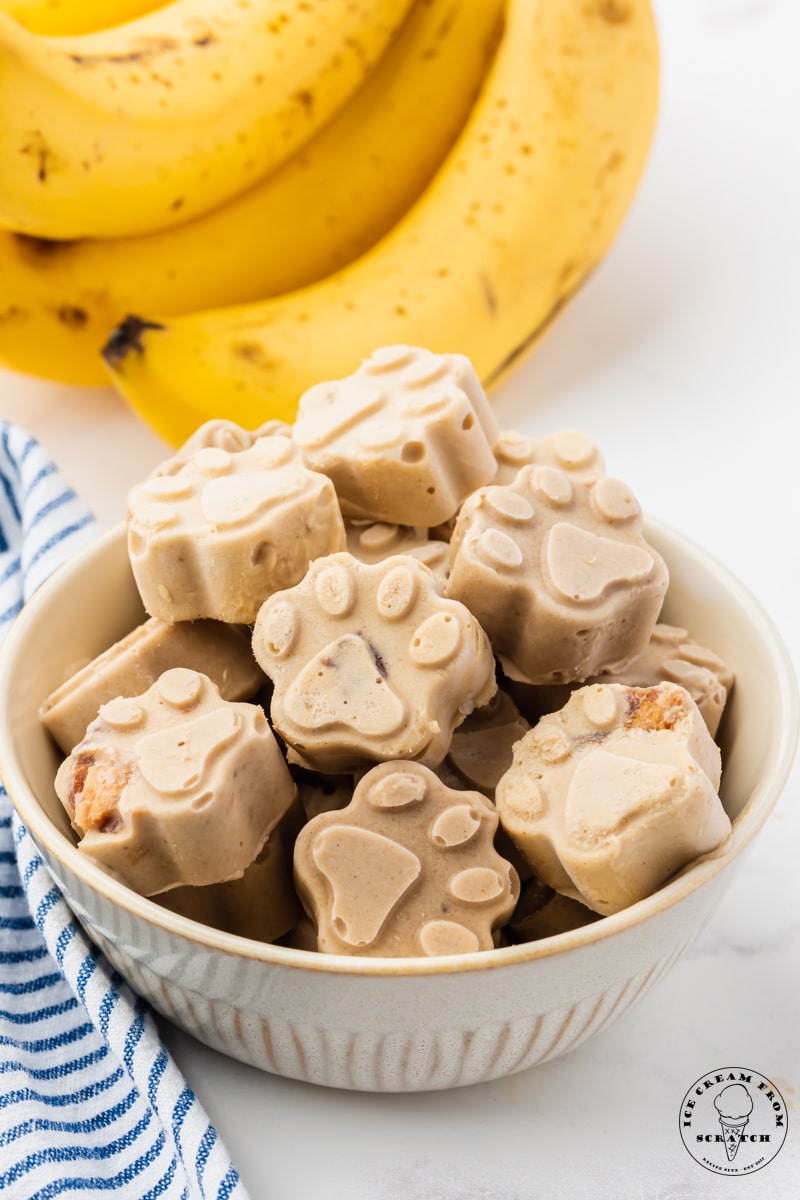 A bowl of dog ice cream treats next to a bunch of yellow bananas.