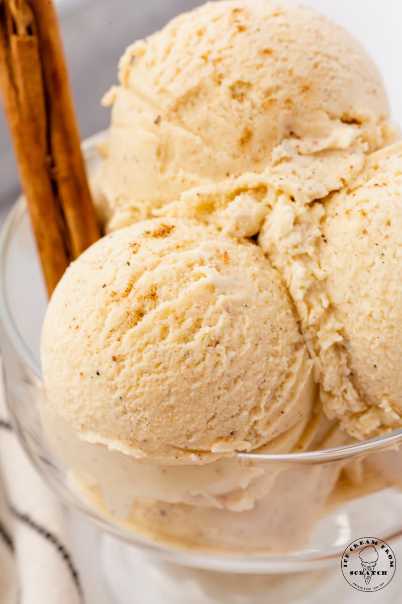 scoops of eggnog ice cream in a glass dish. Cinnamon sticks are garnishing the bowl.