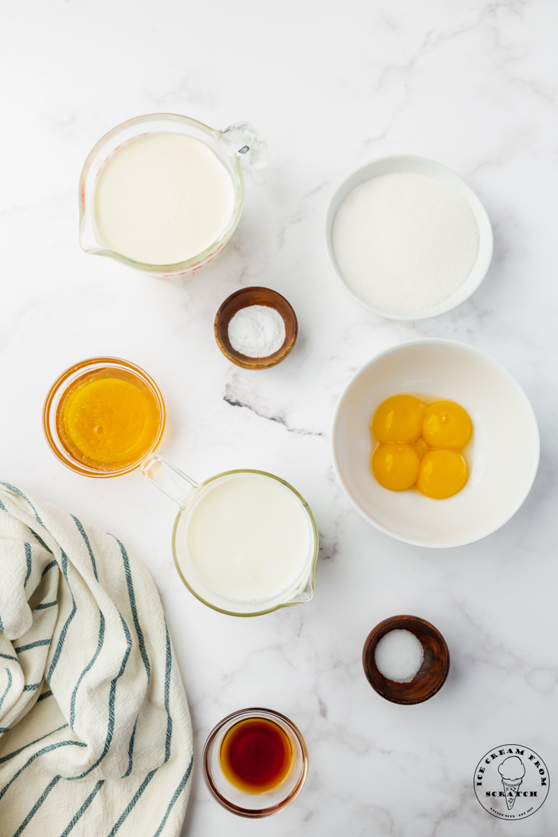 The ingredients needed to make hokey pokey ice cream from scratch, all in small bowls on a marble countertop, viewed from overhead.