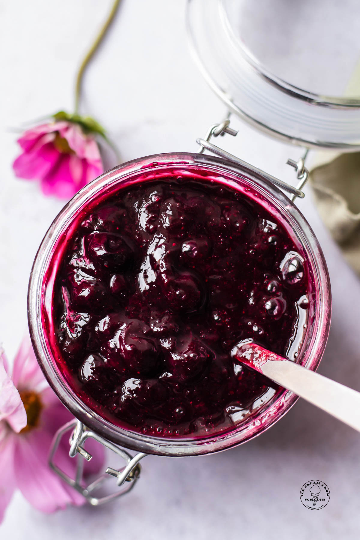 a hinged glass jar of blueberry compote. Purple flowers are seen in the background.