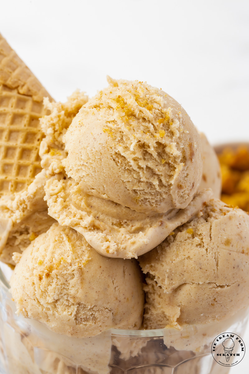 a glass bowl of cookie butter ice cream scoops. a cone is stuck into the scoops upside down.
