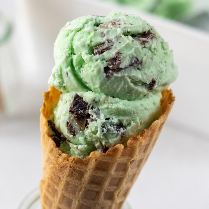 a waffle cone held up in a glass jar filled with scoops of green mint andes chocolate ice cream.