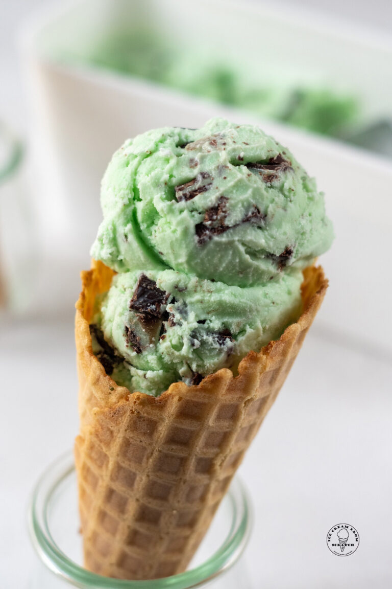 a waffle cone held up in a glass jar filled with scoops of green mint andes chocolate ice cream.