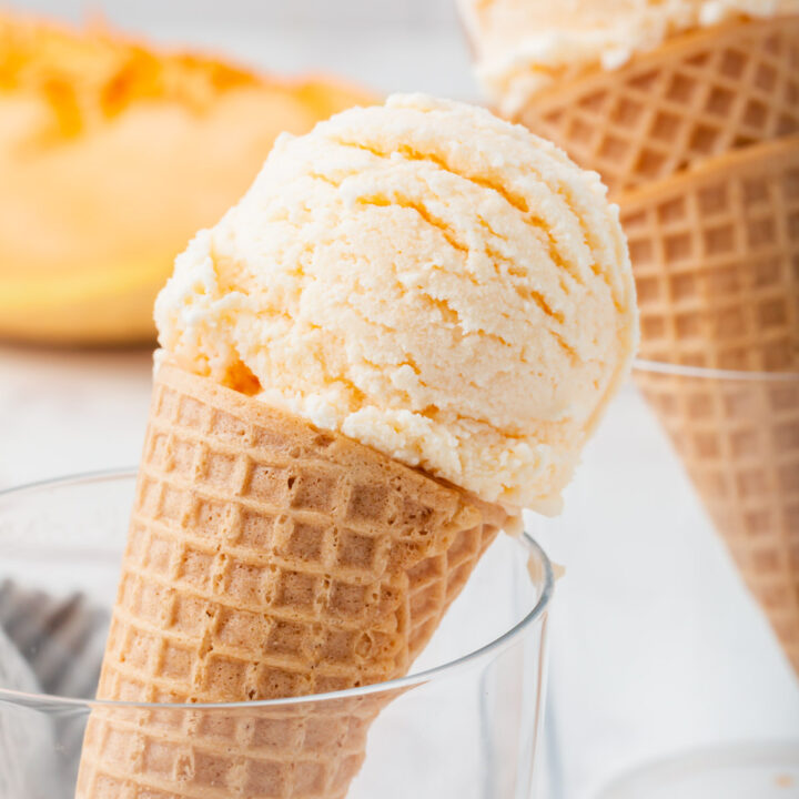 sugar cones topped with scoops of cantaloupe ice cream, propped up in glasses.