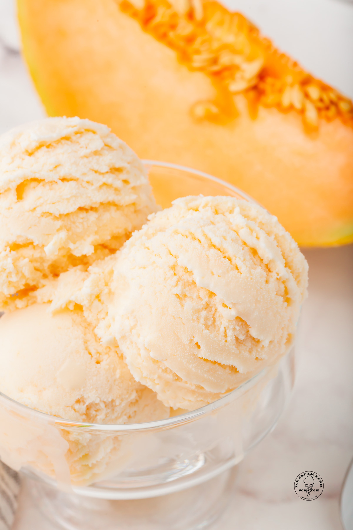 A glass dish filled with scoops of melon ice cream. A large wedge of cantaloupe is in the background.