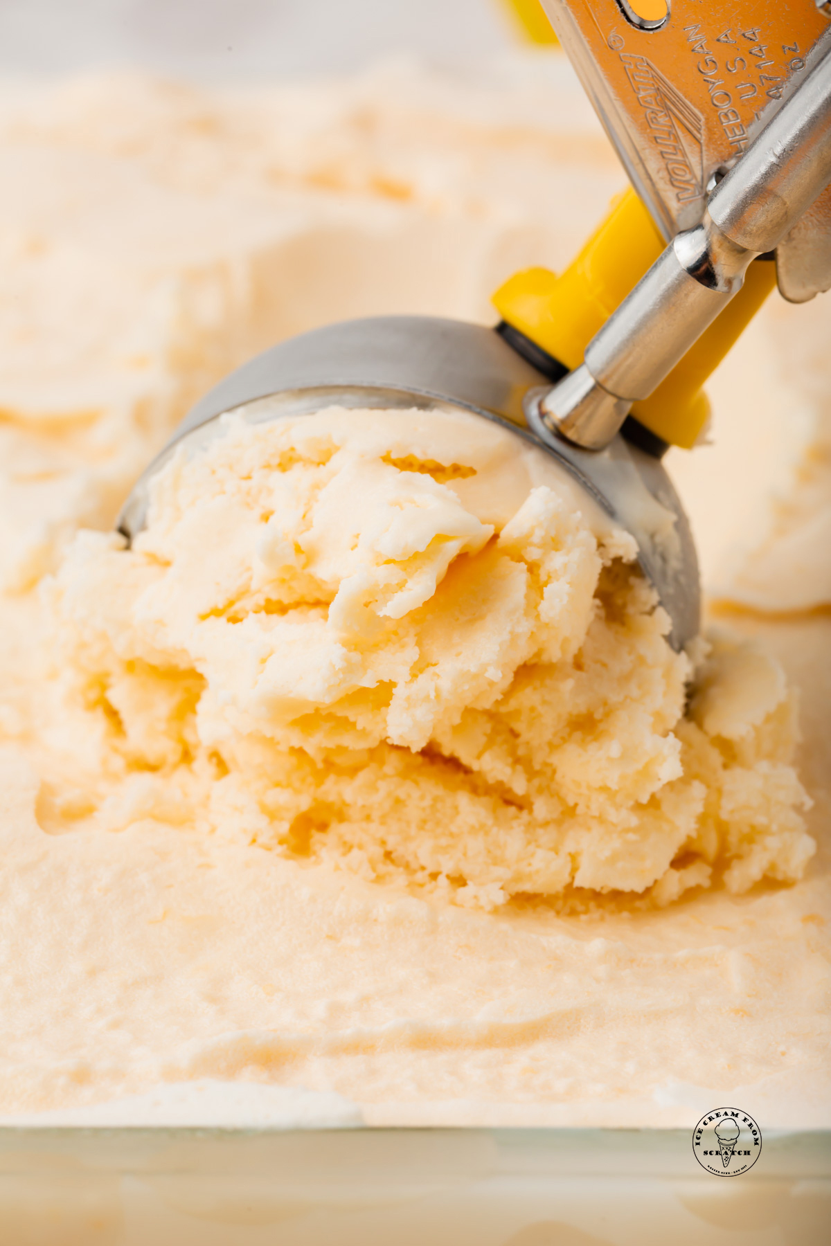 a metal scoop pulling a serving of cantaloupe ice cream from a dish.