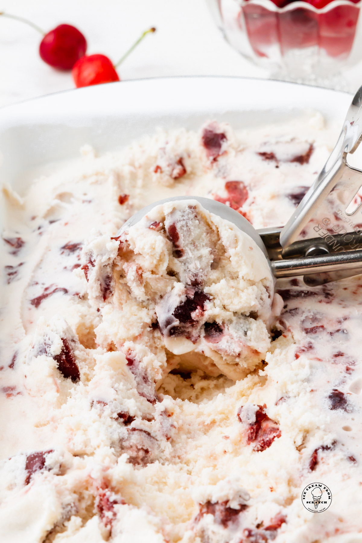 a metal scoop brining up a scoop of homemade cherry gelato from a pan.