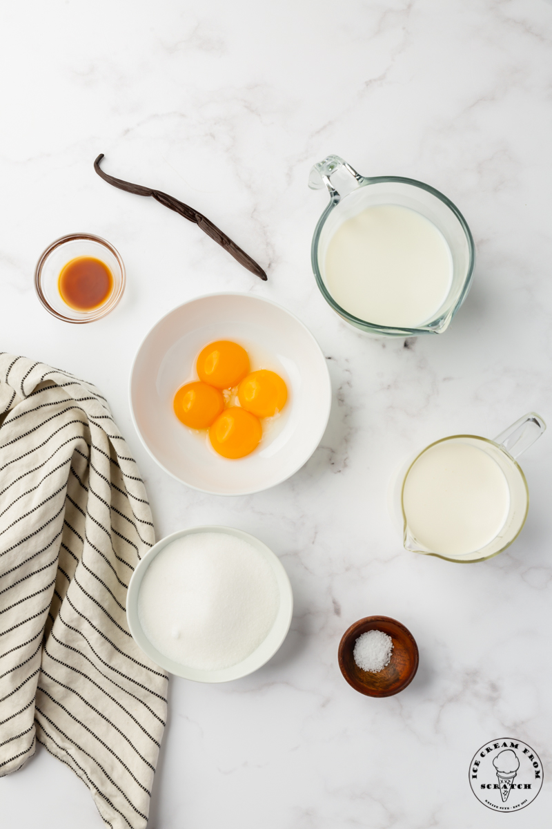 The ingredients needed to make custard style ice cream, in individual bowls on a marble counter.