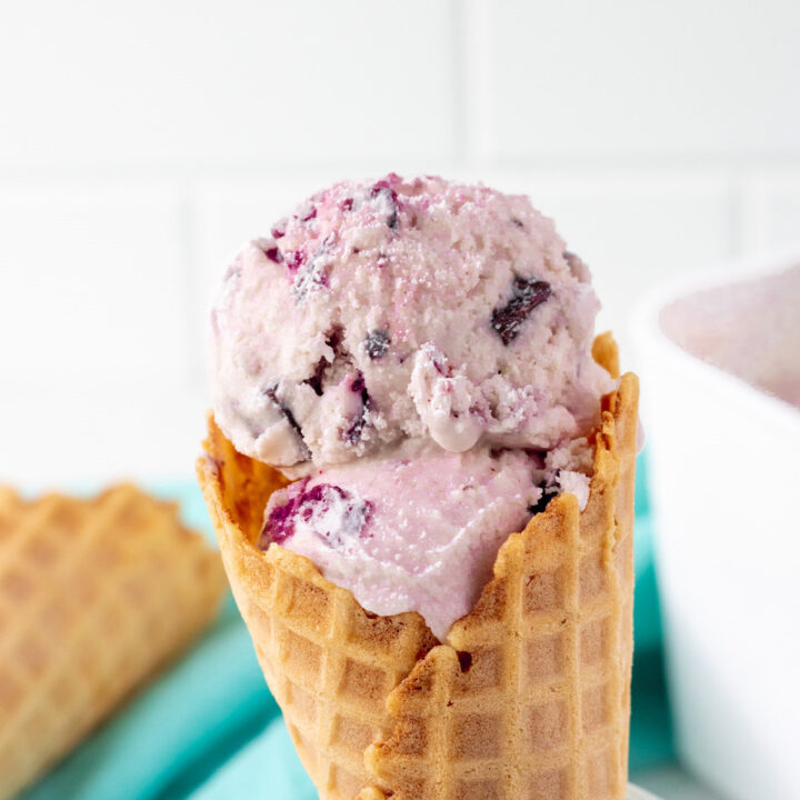 scoops of amaretto ice cream with cherries and chocolate in a waffle cone.
