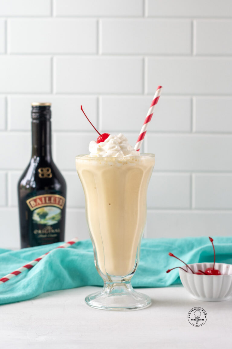 a milkshake in a footed glass with a red and white straw in it, next to a bottle of baileys Irish creme.