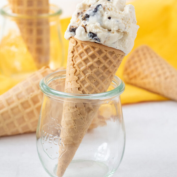 a scoop of homemade butter brickle ice cream on a sugar cone, propped up in a small jelly jar.