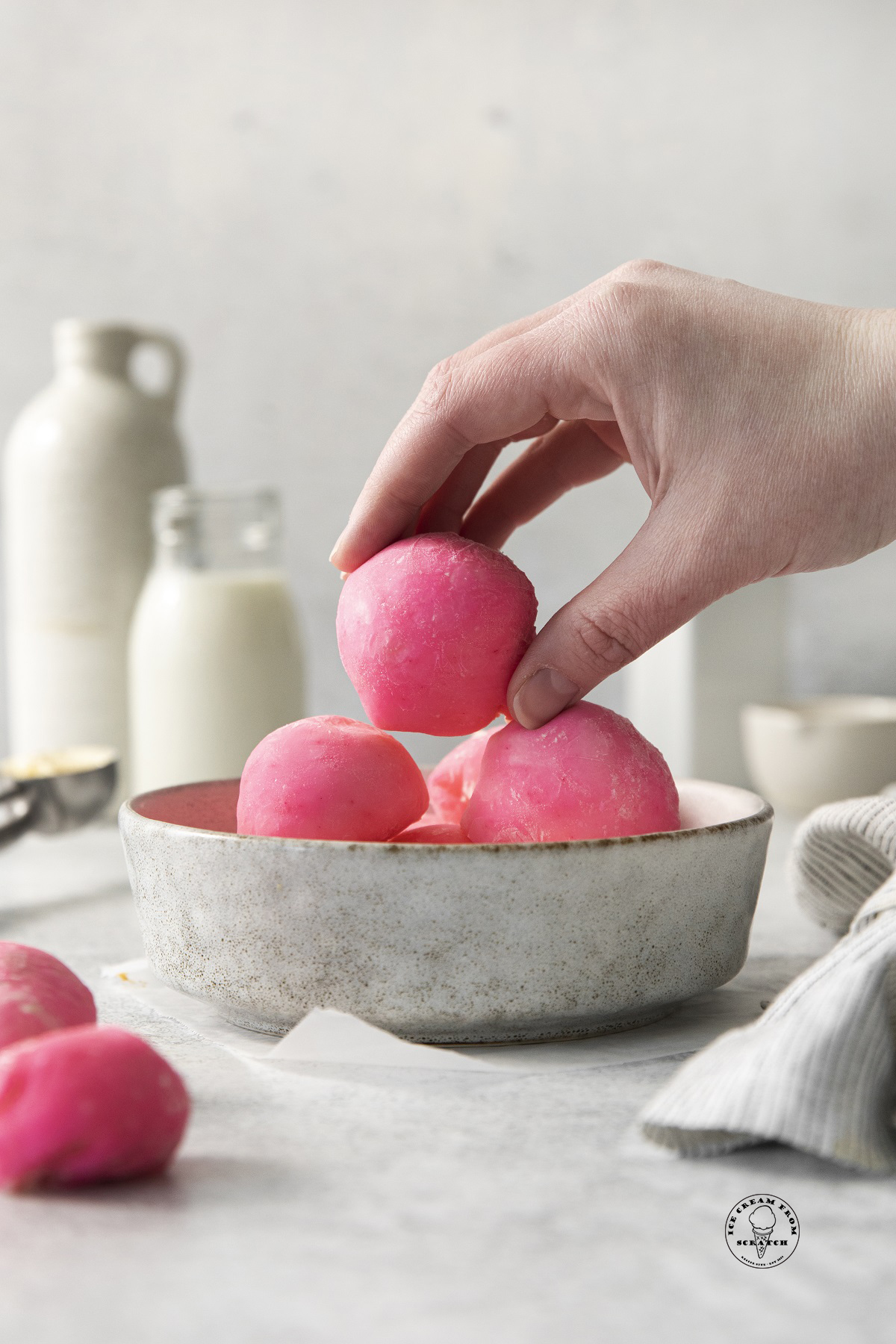 a hand picking up a pink mochi from a bowl